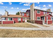 Charming townhouse with red siding, stone chimney, well-maintained lawn, and inviting curb appeal at 8424 Everett Way # E, Arvada, CO 80005