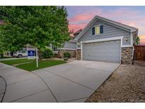 Charming gray home boasting stone accents and a two-car garage, set against a colorful twilight sky at 15502 E Flower Mound Pl, Parker, CO 80134