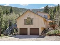 Two-story home featuring a two-car garage and elevated deck access, nestled against a mountainside at 10469 Christopher Dr, Conifer, CO 80433