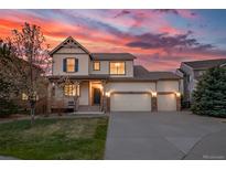 Charming two-story home featuring a three-car garage and covered porch, set against a stunning sunset backdrop at 21482 E Idyllwilde Dr, Parker, CO 80138