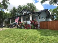 Charming light blue house with lush green lawn, blooming rose bushes, and an American flag on the front porch at 3396 S Logan St, Englewood, CO 80113