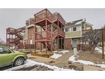 View of townhome complex with red staircases and partial view of green car in snowy parking lot at 970 S Dawson Way # 2, Aurora, CO 80012