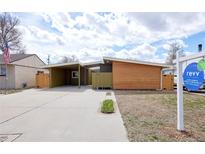 Modern home featuring wooden siding, a carport, and a well-kept concrete driveway with lush green foliage at 5350 E 66Th Way, Commerce City, CO 80022