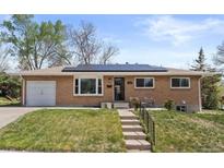 Charming brick ranch-style home featuring a well-manicured lawn, attached garage, and solar panels on the roof at 4102 W Eastman Ave, Denver, CO 80236