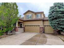 Charming two-story home featuring a three-car garage, a welcoming front porch, and mature trees at 15372 E 117Th Ave, Commerce City, CO 80022
