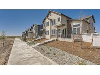 Modern townhome exteriors with light colored wood siding and brick accents along a sidewalk under a bright blue sky at 1224 S Algonquian St, Aurora, CO 80018