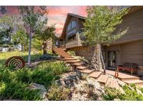Stunning home exterior featuring stone accents, a wooden staircase, and lush landscaping under a vibrant sunset sky at 8361 Piney Creek Rd, Parker, CO 80138