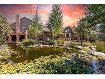 Scenic view of a lovely pond with water lilies in front of a wood and stone home with balconies and mature trees at 8361 Piney Creek Rd, Parker, CO 80138