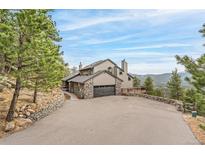 Stunning multi-story home with stone accents, a driveway, and mature trees against a beautiful sky at 3961 Mossy Rock Ln, Evergreen, CO 80439