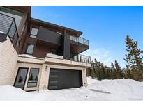Modern three-story home with black garage door, balconies, and stone base amidst a snowy landscape at 436 N Fuller Placer Rd, Breckenridge, CO 80424