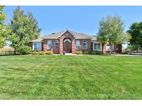 Well-maintained brick home with a manicured lawn and mature trees on a sunny day at 18399 Wagon Trl, Mead, CO 80542