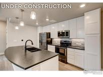 Modern kitchen features stainless steel appliances, white cabinets, and a black countertop island at 265 High Point Dr # 203, Longmont, CO 80504