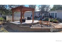 Charming backyard with a wooden pergola, brick retaining wall, and lovely landscaping, great for outdoor living at 10635 County Road 24, Fort Lupton, CO 80621