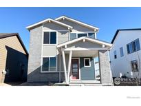 Charming two-story home features gray brick and siding, complemented by a welcoming front porch and a colorful red door at 2283 Serenidad St, Brighton, CO 80601