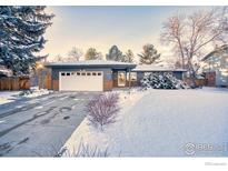 Ranch style home with attached garage, snowy lawn, and mature trees at 1701 Harvard St, Longmont, CO 80503