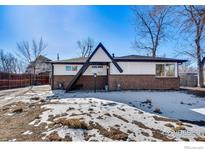 Brick ranch home with a modern A-frame entryway, snowy front yard, and mature trees at 10690 W 47Th Pl, Wheat Ridge, CO 80033