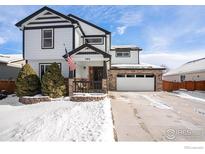 Charming two-story home featuring an American flag, a brick-accented garage, and a snowy front yard at 580 Mount Massive St, Berthoud, CO 80513