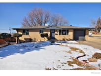 Charming brick home with blue trim, attached garage and a yard partially covered in snow on a sunny day at 6487 Eaton St, Arvada, CO 80003