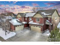 Charming townhomes featuring attached garages, stone accents and snow-covered roofs under a dramatic sky at 2128 Calais Dr # B, Longmont, CO 80504