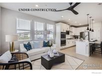 Bright, open-concept living room flows into a modern kitchen with white cabinets and island seating at 2747 Bear Springs Cir, Longmont, CO 80503