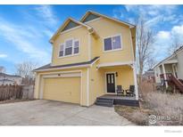 Charming yellow two-story home featuring a black door and inviting front porch, with an attached garage at 740 Boxwood Ln, Longmont, CO 80503