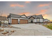 Beautiful modern farmhouse with wood-accented garage doors and a spacious driveway under a colorful sunset at 1291 Swan Peter Dr, Berthoud, CO 80513