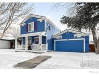 Charming blue two-story home with a covered front porch and attached garage, all surrounded by a snowy landscape at 380 Tynan Dr, Erie, CO 80516