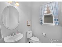 Bright bathroom featuring a pedestal sink, toilet, and a window with blue and white striped curtains at 887 Sundance Ln, Erie, CO 80516