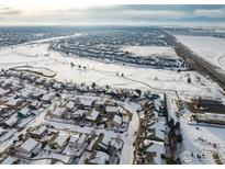 Snowy aerial view of a residential community featuring single-Gathering homes, a golf course, and mountain views at 2429 Tyrrhenian Dr, Longmont, CO 80504