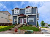 Inviting blue townhome featuring a well-manicured lawn and colorful flower beds leading to the front doors at 711 Elm St, Frederick, CO 80530