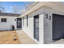 Charming front exterior featuring painted brick, well-manicured lawn, and a dark gray garage door at 23 Durian Ct, Longmont, CO 80503