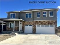 Two-story home featuring gray siding and a brick facade, complemented by a two-car garage and a well-lit porch at 1866 Sawtooth Mountain Dr, Berthoud, CO 80513