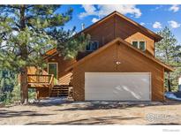 Beautiful, sunlit two-story home featuring a garage and elevated porch with green door nestled in a wooded landscape at 333 Antler Dr, Boulder, CO 80302