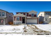 Two-story home featuring a two-car garage, stone accents, and a well-maintained front yard with snowy landscaping at 6121 Easton Cir, Frederick, CO 80504