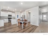 Open-concept kitchen with stainless steel appliances, white cabinets, and eat-in dining area at 2539 Alto St, Fort Lupton, CO 80621