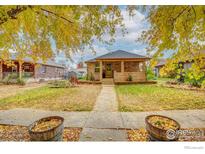 Charming brick home featuring a covered porch and mature trees in a well-manicured front yard at 109 E Iowa Ave, Berthoud, CO 80513