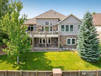 Expansive backyard featuring a patio, lush lawn, mature trees and a stone-accented home exterior, perfect for outdoor living at 13943 W 87Th Ln, Arvada, CO 80005