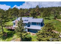 Charming two-story home with blue siding, stone chimney, and spacious deck nestled among mature trees at 8483 Thunderhead Dr, Boulder, CO 80302