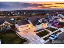 Stunning aerial view of a modern home with three-car garage, lush landscaping, and neighborhood setting at sunset at 405 Buckskin Rd, Berthoud, CO 80513