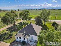 Aerial view of charming white house with dark roof surrounded by lush green trees and fields against a mountain backdrop at 14798 N 115Th St, Longmont, CO 80504