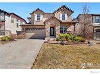 Two story home with a beige exterior, stone accents, two car garage, manicured lawn, and a concrete driveway at 8426 Wilkerson Ct, Arvada, CO 80007