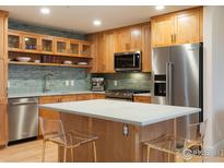 Modern kitchen with stainless steel appliances, wood cabinets, an island, and a green tiled backsplash at 3701 Arapahoe Ave # 304, Boulder, CO 80303