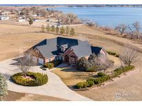 Stunning aerial view of brick home with mature landscaping, circular driveway, and a picturesque lake backdrop at 2366 Shoreside Dr, Berthoud, CO 80513