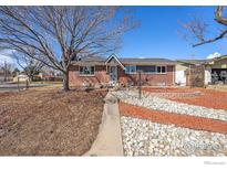 Charming single-Gathering home with red brick exterior, landscaped front yard, and mature trees on a sunny day at 4105 Yarrow Ct, Wheat Ridge, CO 80033