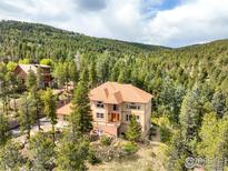 Beautiful three-story home with a large yard and a deck surrounded by lush greenery and mature trees at 12023 Coal Creek Heights Dr, Golden, CO 80403