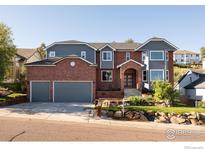 Striking two-story home featuring a brick facade, grey siding, a two-car garage, and manicured landscaping at 16078 W Ellsworth Dr, Golden, CO 80401