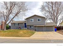 Charming gray two-story home with a three-car garage, blue door, and mature trees at 2136 S Balsam Ct, Lakewood, CO 80227