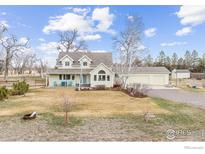 Charming two-story home featuring a welcoming front porch and mature trees on a sunny, landscaped lawn at 7430 Cardinal Ln, Longmont, CO 80503