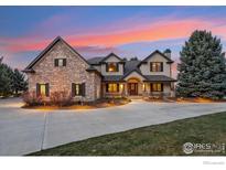 Stunning stone home with manicured lawn, circular drive, and sunset sky at 9092 Fieldcrest Ln, Longmont, CO 80503