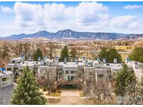 Lovely exterior view of a multi-unit property, backing to mature trees and a mountain backdrop on a sunny day at 3260 47Th St # 206A, Boulder, CO 80301